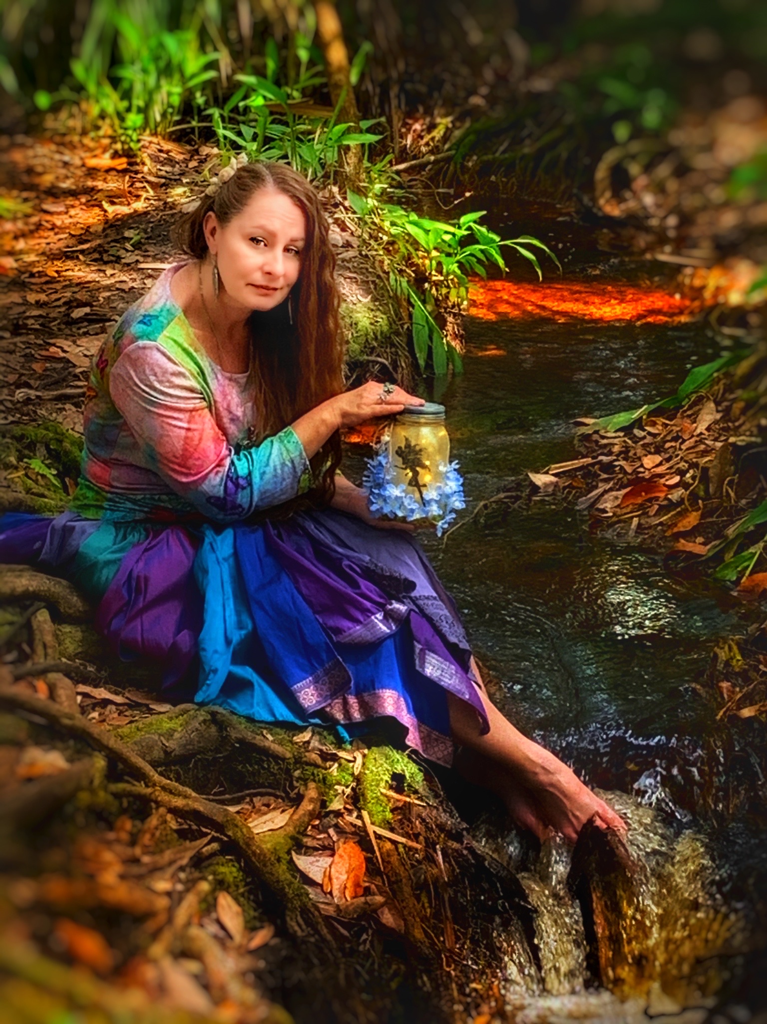 Artist sitting near wooded stream holding luminary jar.