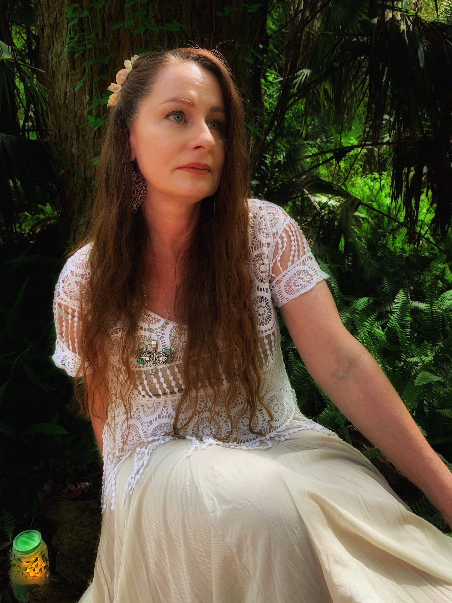 Artist sitting near wooded stream holding luminary jar.